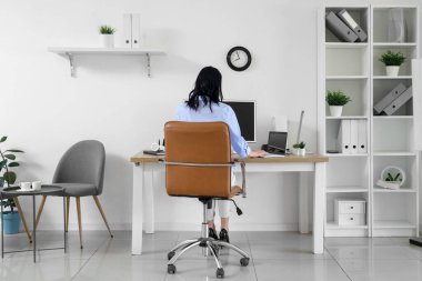 İş yerinde çalışan genç bir kadın modern bilgisayar ve dizüstü bilgisayarla aydınlık ofiste çalışıyor.