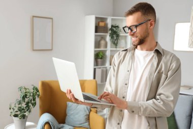 Gözlüklü genç adam evde dizüstü bilgisayar kullanıyor.