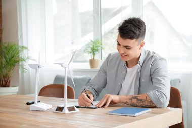 Ofiste çalışan rüzgar türbini modelli genç adam.