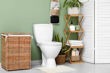 Tuvaletin içinde klozet, raf ünitesi, çamaşır sepeti ve yeşil duvarın yanında organizatör var.