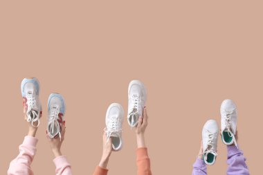 Bej arka planda farklı spor ayakkabıları olan kadın elleri.