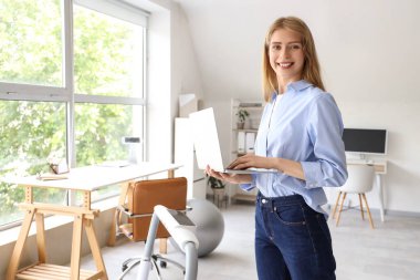 Genç iş kadını ofiste dizüstü bilgisayarla çalışıyor.