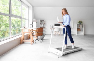 Ofiste koşu bandında dizüstü bilgisayar eğitimi alan genç bir iş kadını.