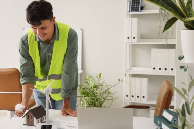 Ofisteki masasında ampul, ev ve rüzgar türbini modeli olan erkek mühendis