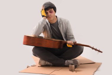 Gitarlı genç evsiz bir adam kartonda oturuyor.