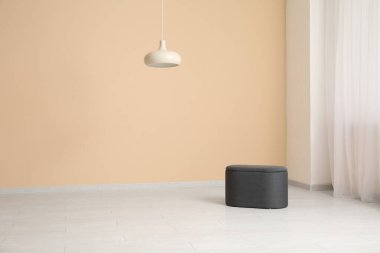 Boş odadaki bej duvarın yanında asılı lamba ve puf.