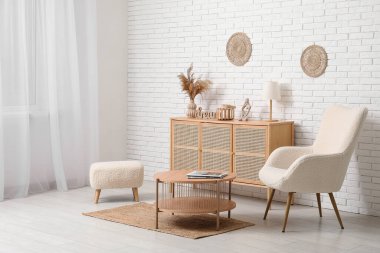 Dekor, koltuk, sehpa ve beyaz tuğla duvarın yanında puf olan modern çekmeceler.