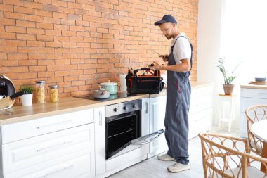 Mutfakta fırını tamir eden alet çantalı bir erkek teknisyen.