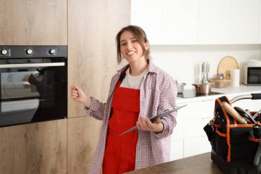 Mutfakta elektrikli fırının yanında panosu olan kadın teknisyen.