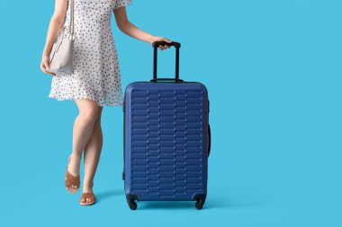 Mavi arka planda bavulu ve çantası olan genç bir kadın.