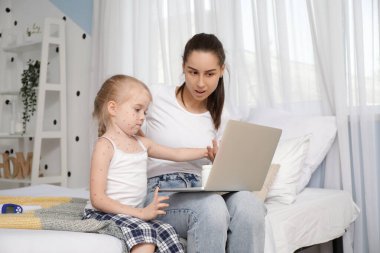 Suçiçeği hastası küçük bir kız ve annesi yatak odasında video sohbeti yapıyor.