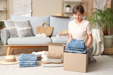 Kadın evde temiz kıyafetleri karton kutulara katlıyor.