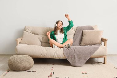 Kulaklıklı güzel bir kadın evdeki gri kanepede müzik dinliyor.