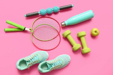Elma, spor ayakkabısı ve pembe arka planda farklı spor aletleri.