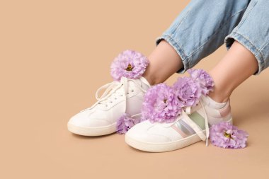 Bej arka planda Eustoma çiçekleri olan spor ayakkabılı genç kadın bacakları.