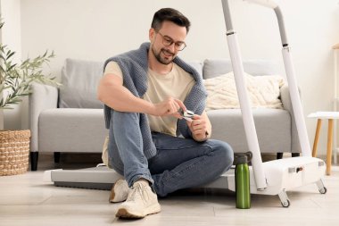 Nabız oksimetresi olan genç bir adam evde yerde oturuyor.