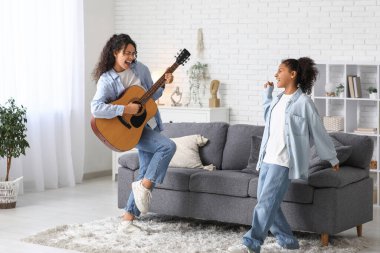 Güzel, mutlu, Afro-Amerikan bir anne kızına evde gitar çalmayı öğretiyor.