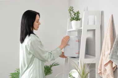 Genç bir kadın banyoda kozmetik buzdolabı açıyor.