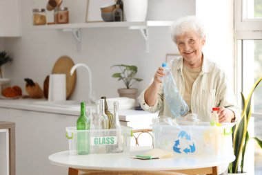 Mutfakta elinde çöp bidonları olan yaşlı bir kadın. Atık sıralama kavramı