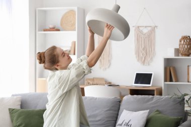 Genç bir kadın evdeki lambaya ampul takıyor.