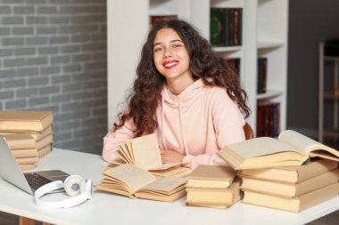 Bayan öğrenci kütüphanede dizüstü bilgisayarla masada ders çalışıyor.