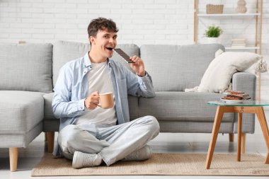 Tatlı çikolatalı yakışıklı genç adam ve bir fincan kahve oturma odasında halının üzerinde oturuyor.