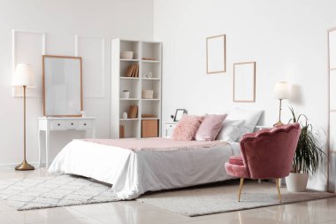 Rahat yatağı, yumuşak koltuğu ve beyaz duvarında resim çerçeveleri olan şık bir yatak odası.