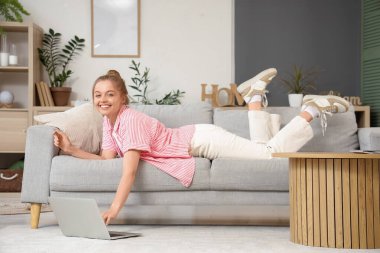 Evdeki koltukta modern laptop kullanan genç bir kadın.