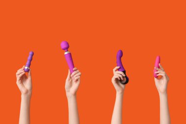 Turuncu arka planda farklı vibratörlere sahip kadın elleri.
