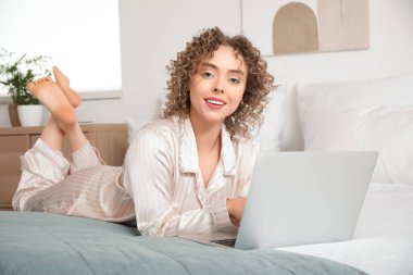 Yatak odasında dizüstü bilgisayarı olan genç bir kadın.