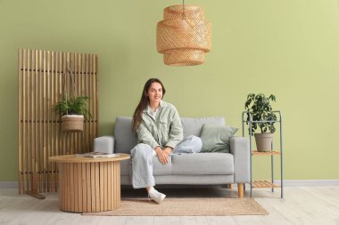 Evdeki gri kanepede dinlenen genç ve güzel bir kadın.