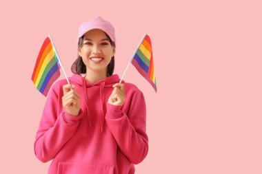 Beautiful young woman with LGBT flags on pink background