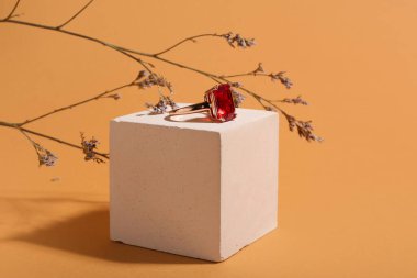 Turuncu arka planda dekoratif podyumda kırmızı mücevherli güzel bir yüzük. Yakın çekim.