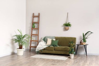 Oturma odasının içinde kanepe, merdiven, masa ve beyaz duvarın yanında farklı bitkiler var.