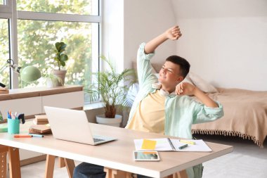 Mutlu genç çocuk yatak odasındaki masada ders çalışıyor.