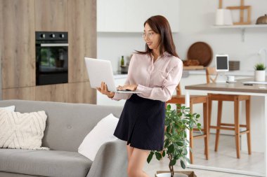 Genç Asyalı iş kadını mutfakta dizüstü bilgisayarla çalışıyor.