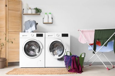 Çamaşır makinesi, kurutma makinesi ve çamaşır sepetinin olduğu banyonun içi.