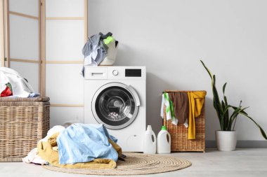 Çamaşır makinesi, kirli çamaşırlar ve çamaşır sepetinin olduğu hafif banyonun içi.