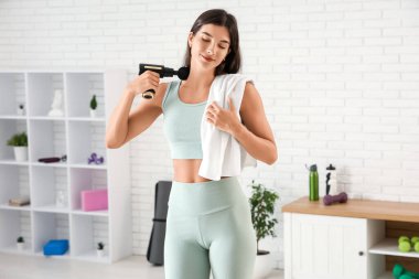 Spor salonundaki eğitimden sonra vurmalı masaj aleti kullanan genç bir kadın.