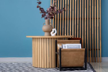 Kahve masasının üzerinde vazoda okaliptüs dalları ve odadaki mavi duvarın yanında dergi tutacağı.