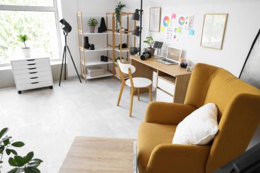 Modern fotoğraf stüdyosunda koltuk, dizüstü bilgisayar ve ışıklandırma ekipmanlarıyla fotoğrafçılık.