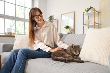 Evdeki kanepede oturan sevimli kedisi olan güzel, genç ve mutlu bir kadın.