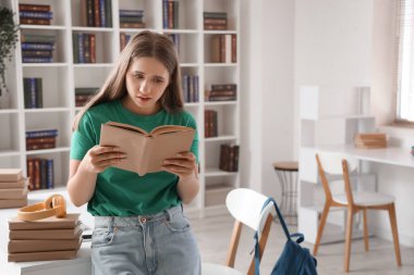 Kütüphanede ders çalışırken kulaklıkla kitap okuyan şok olmuş bir kız öğrenci.