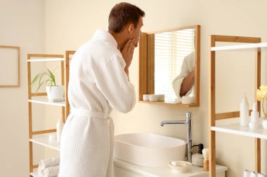 Genç adam duştan sonra aynaya bakıyor.