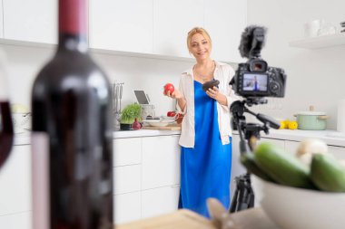 Mutfakta sebzeli olgun bir kadın yemek pişirme kursunu kaydediyor.