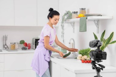 Genç bir kadın mutfakta yemek pişirirken salatalık yıkıyor.