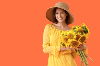 Hasır şapkalı, turuncu arka planda bir buket ayçiçeği olan güzel, genç ve mutlu bir kadın.