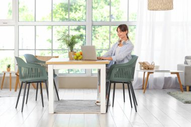 Yemek odasında dizüstü bilgisayar kullanan genç bir kadın.