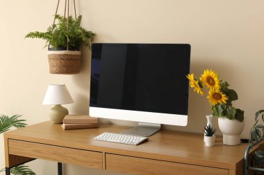 Modern bilgisayarı, kitapları ve bej duvarın yanında ayçiçekleri olan güzel bir iş yeri.