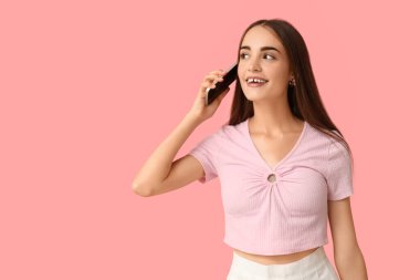Diyastemalı genç bir kadın pembe arka planda cep telefonuyla konuşuyor.